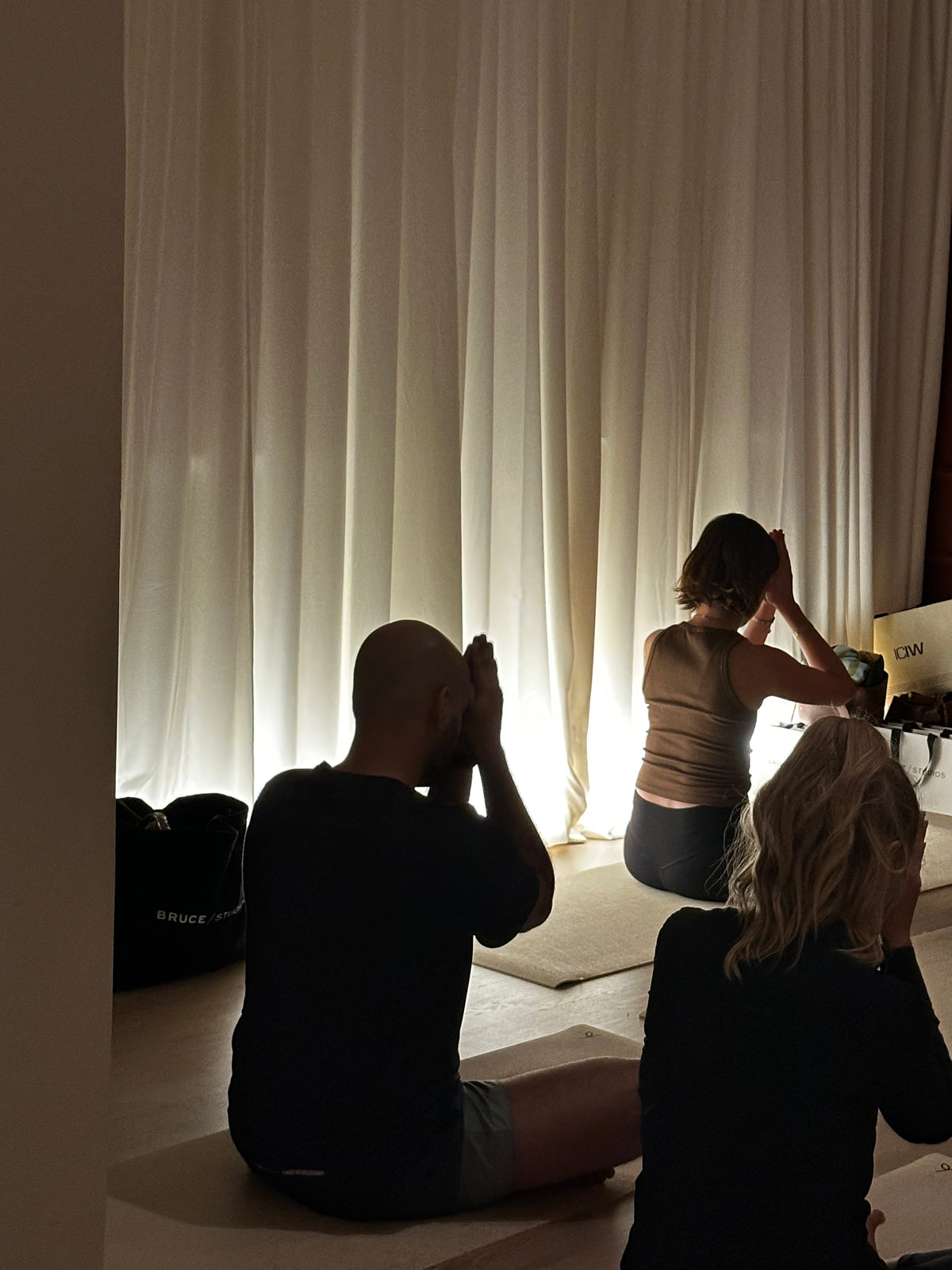 Tre deltagare i sittande meditation mot en upplyst gardin
